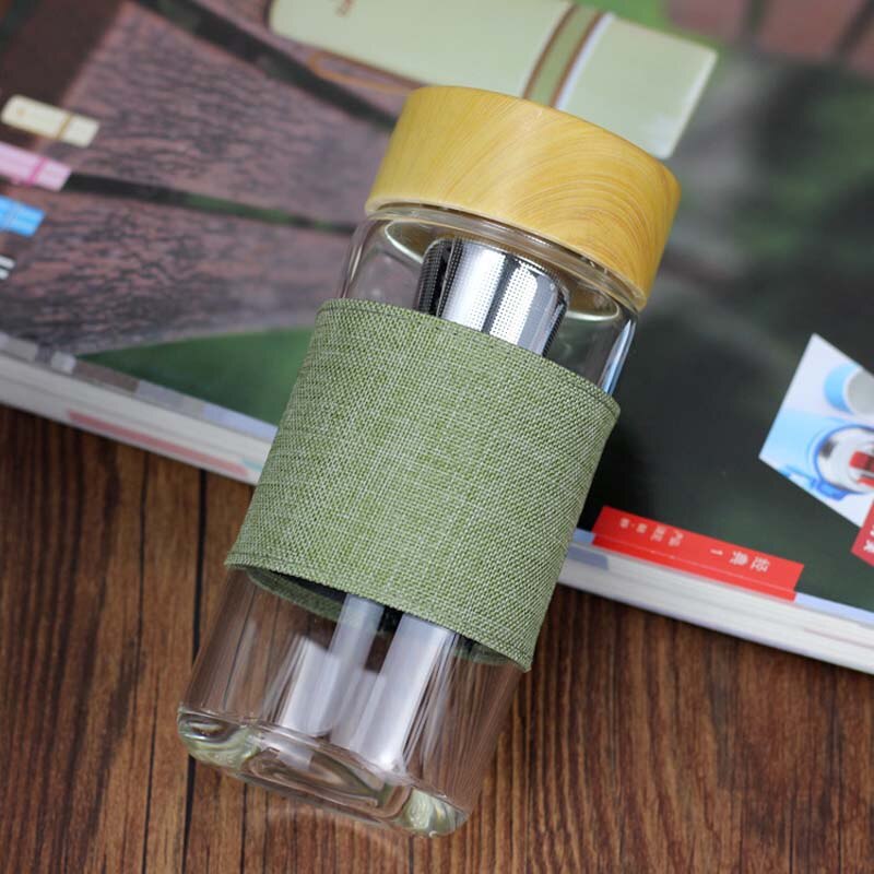 Eine durchsichtige Glas-Trinkflasche mit einem Bambusdeckel und einem gruenen Stoffband in der Mitte, dass auf  Buechern liegt.