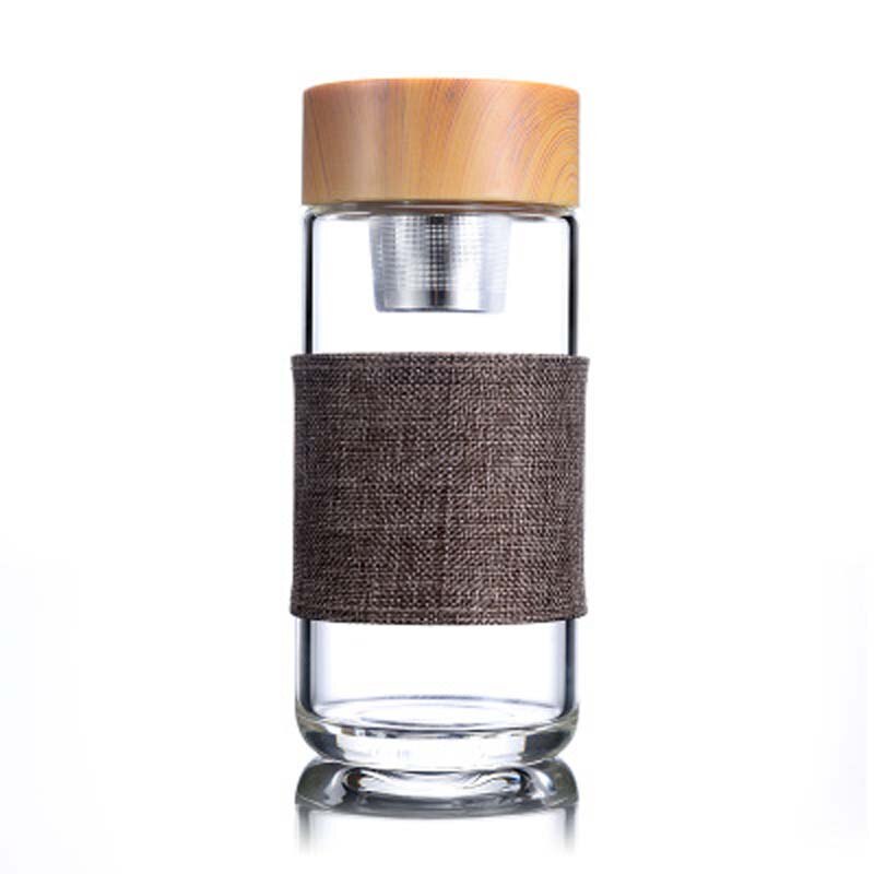 Eine transparente Glas-Trinkflasche mit einem Teesieb und einem Bambusdeckel, umgeben von einem braunen Stoffband, vor einem weissen Hintergrund.
