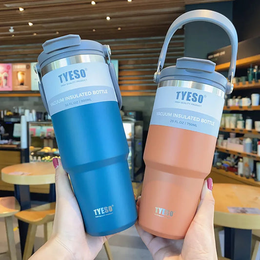 Zwei vakuumisolierte Trinkflaschen, eine in Blau mit einem Volumen von 900 ml und die andere in Orange mit einem Volumen von 750 ml, gehalten in Haenden vor einem Café-Hintergrund. Beide Flaschen haben einen grauen Deckel mit Tragegriff.