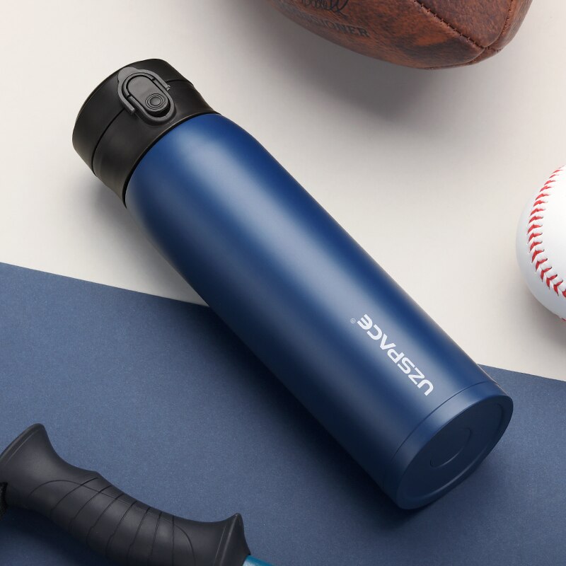 Eine blaue Edelstahl-Thermosflasche auf einem dunkelblauen Untergrund, neben einem Baseball und einem Teil eines Basketballs.