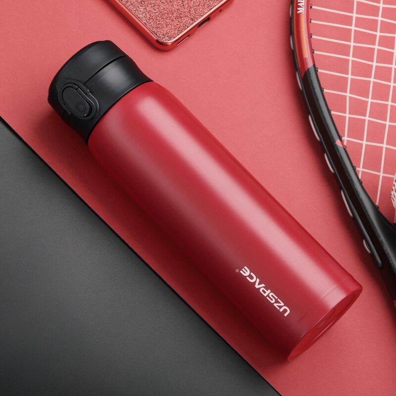 Eine rote Edelstahl-Thermosflasche mit einem schwarzen Deckel, neben einem Tennisschlaeger und einem Smartphone auf einem rot-schwarzen Hintergrund.