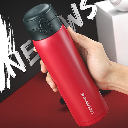 Eine rote Edelstahl-Thermosflasche mit einem schwarzen Deckel, die von einer Hand gehalten wird, vor einem Hintergrund mit der Aufschrift "NEWS".