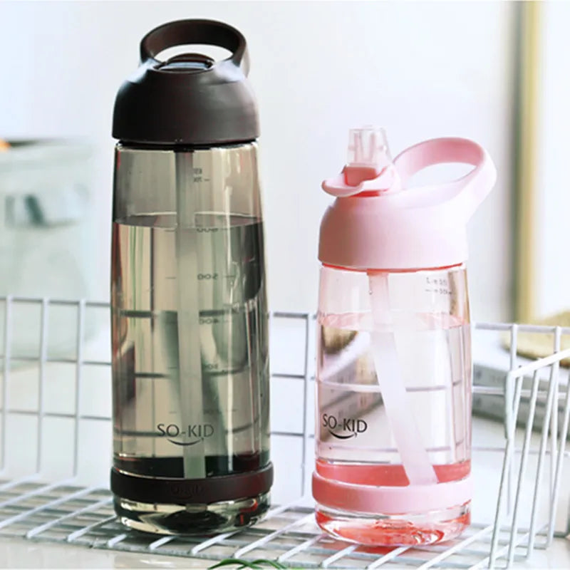 Zwei transparente Kinder-Trinkflaschen, eine in Schwarz und eine in Pink, stehen nebeneinander auf einem Gitter.
