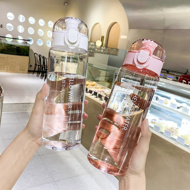 Zwei durchsichtige Wasserflaschen, eine mit weissem und eine mit rosa Deckel, gehalten in Haenden vor einem Café-Hintergrund.