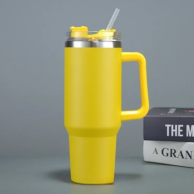 Eine gelbe Thermosflasche mit Strohhalm und einem großen Griff, platziert neben einem Buch auf einem grauen Hintergrund.