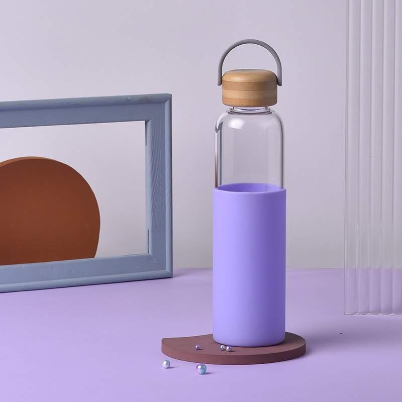 Stehende Glasflasche mit lila Silikonschutz und Bambusdeckel auf einer braunen Oberflaeche, vor einem Spiegel.