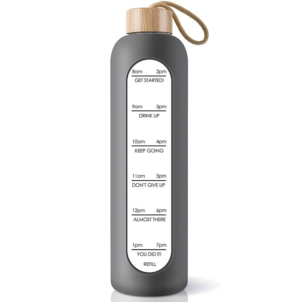 Eine graue Glastrinkflasche mit Zeitmarkierungen und einem Bambusdeckel, versehen mit einem Jute-Trageband.
