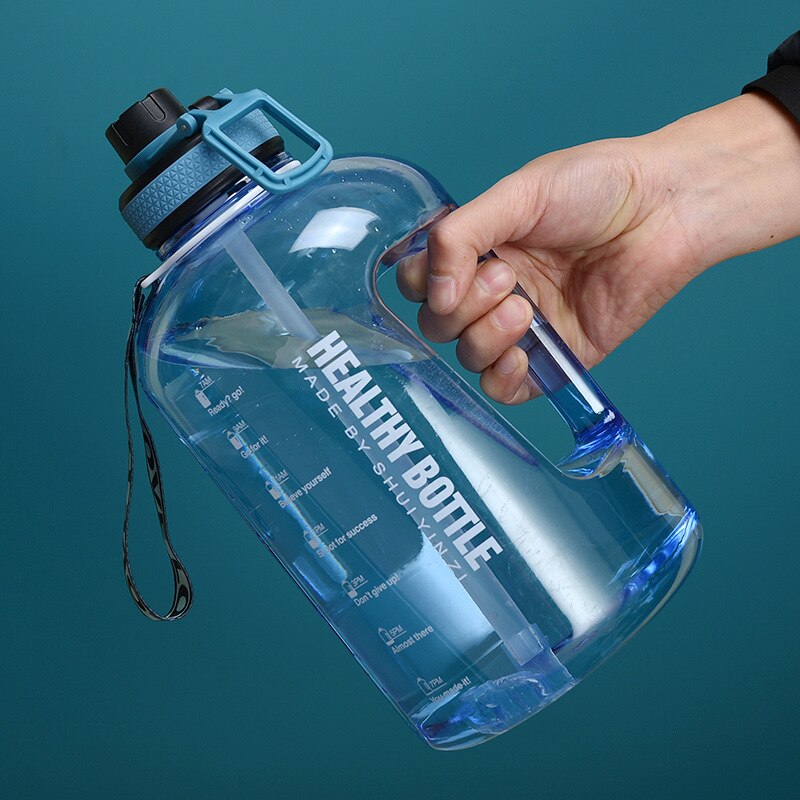 Eine Hand haelt eine grosse, transparente blaue Sporttrinkflasche mit einem Henkel und aufgedrucktem Text "HEALTHY BOTTLE" und motivierenden Slogans zur Wasseraufnahme.