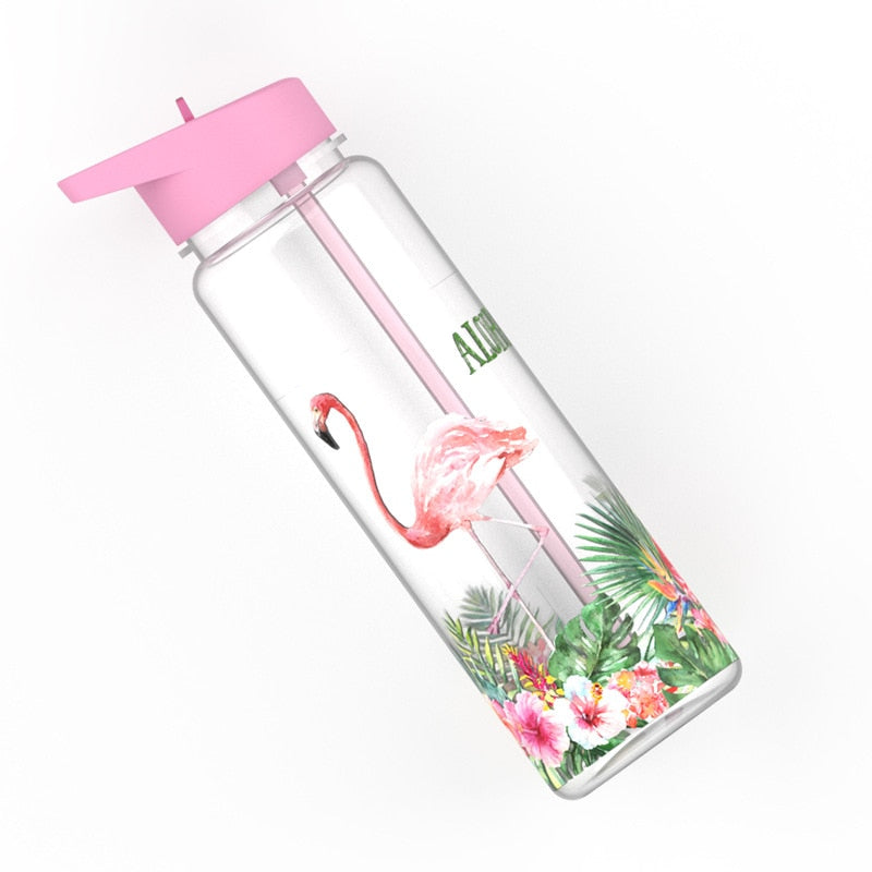 Eine transparente Kindertrinkflasche mit einem rosafarbenen Deckel und einem Flamingo-Design, umgeben von tropischen Pflanzen.