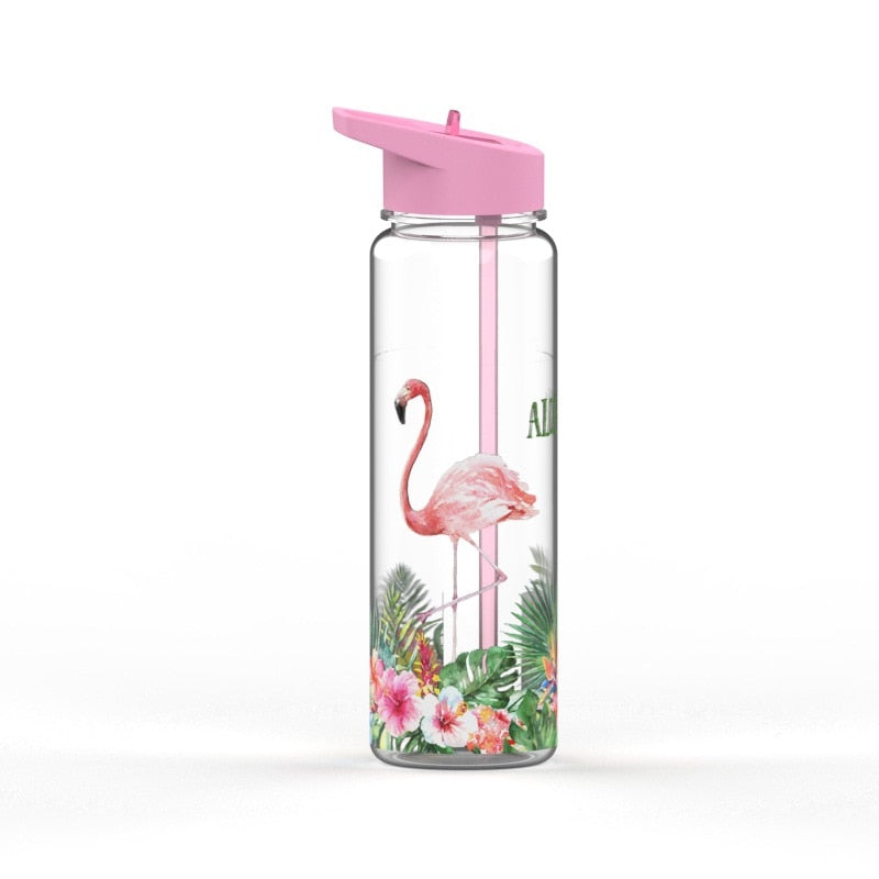 Eine transparente Kindertrinkflasche mit einem rosafarbenen Deckel und einem Flamingo-Design, umgeben von tropischen Pflanzen.