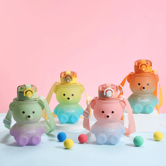 Vier bunte Teddybaer-Trinkflaschen mit der Aufschrift "Smile". Sie sind in verschiedenen Farben (gruen, gelb, rosa und blau) dargestellt und mit passenden Tragegurten versehen. Im Vordergrund liegen bunte Baelle. Der Hintergrund ist rosa und tuerkis.