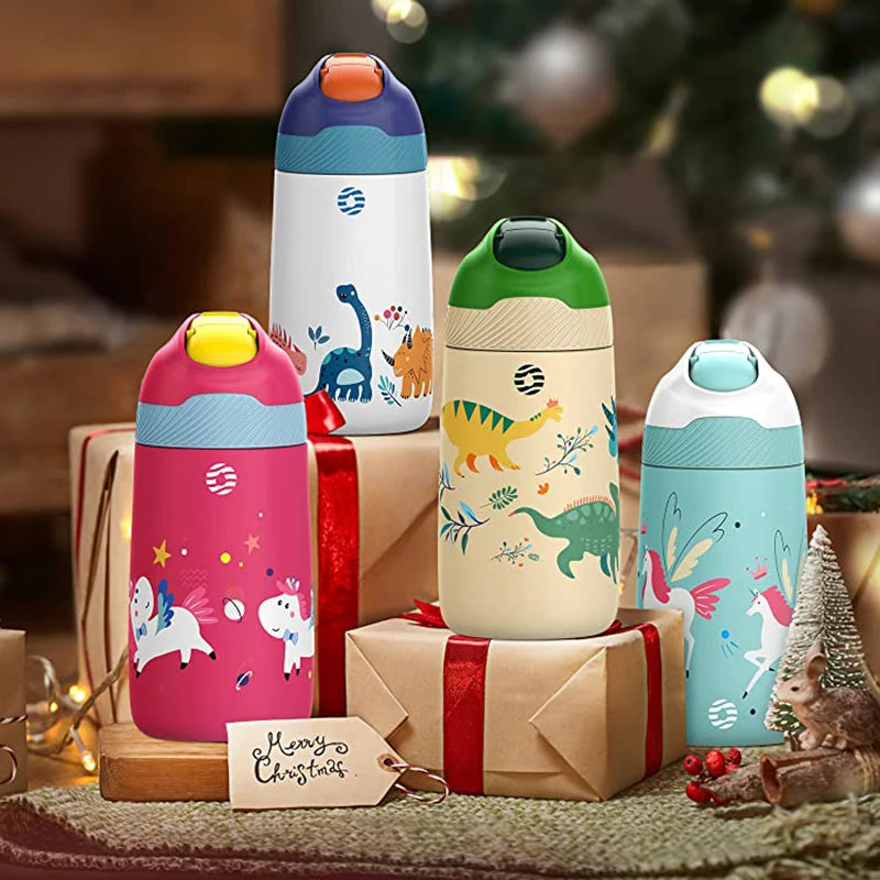 Farbige Kinder-Thermosflaschen mit Tiermotiven, arrangiert auf einem weihnachtlich dekorierten Tisch mit Geschenken, Lichterketten und einer Grußkarte mit der Aufschrift "Merry Christmas".