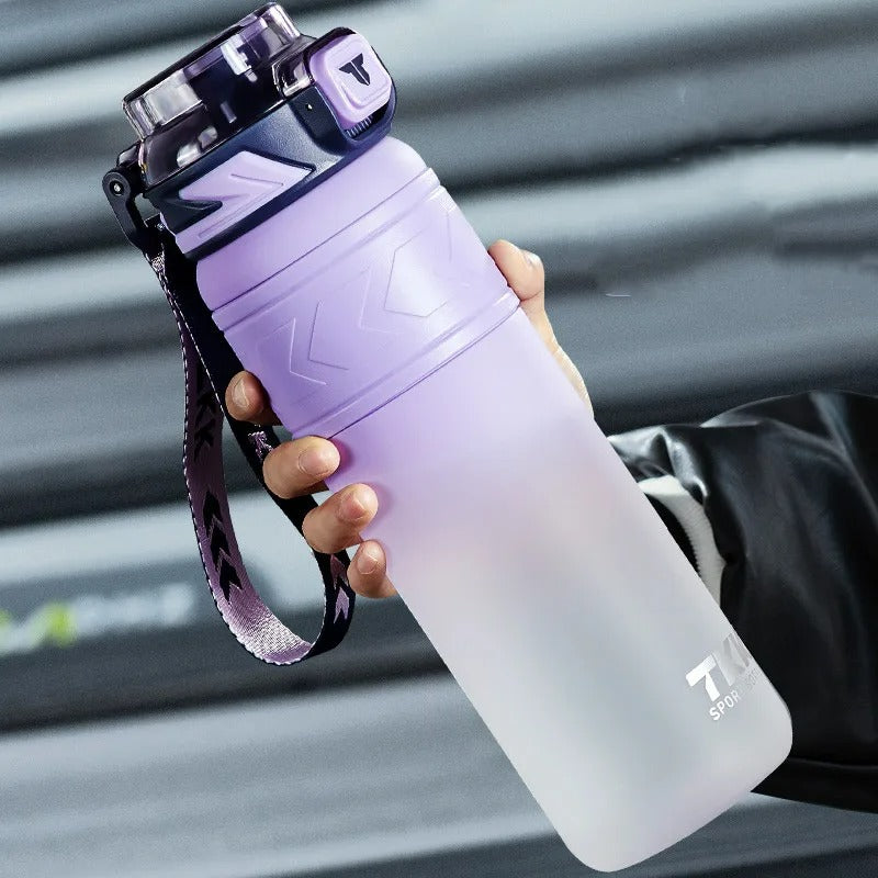 Violett-weisse Sport-Trinkflasche mit 1 Liter Fassungsvermoegen und integriertem Strohhalm. Sie ist mit einem praktischen Tragegriff und einem violett-weissem Trageband ausgestattet. Die Flasche wird gehalten und ist vor einem unscharfen, grauen Hintergrund positioniert.