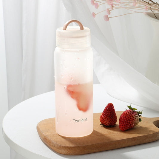 Milchige Glasflasche mit rosa Getraenk und Erdbeeren, beschriftet mit 'Twilight', auf einem Holzbrett neben einem Fenster mit weißen Vorhaengen.