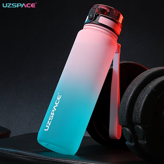 Eine Sporttrinkflasche mit einem Farbverlauf von Pink zu Blau neben Gewichtheberausruestung. Die Flasche traegt das Logo "UZSPACE" und ist mit einem praktischen Trageriemen ausgestattet.