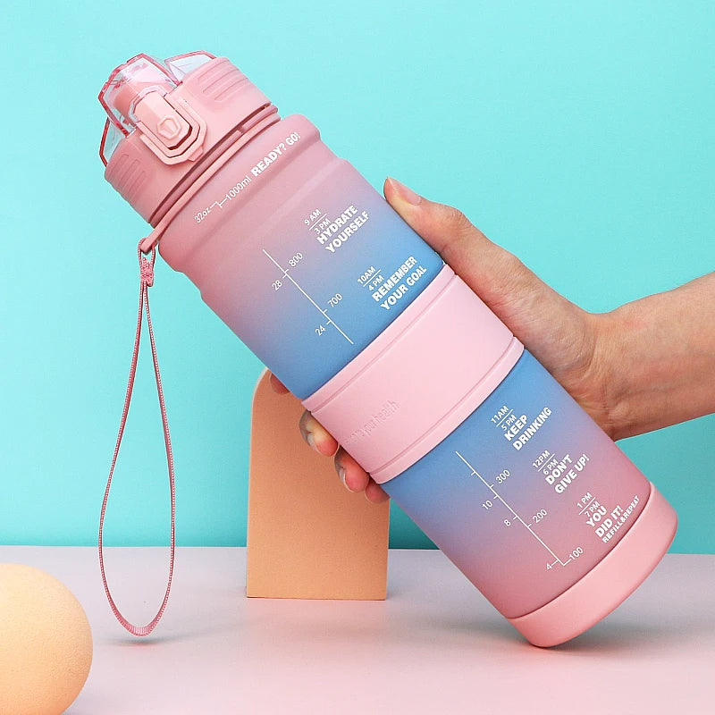 Eine Hand haelt eine pink-blaue Wasserflasche mit Zeitmarkierungen und motivierenden Nachrichten gegen einen hellblauen Hintergrund.