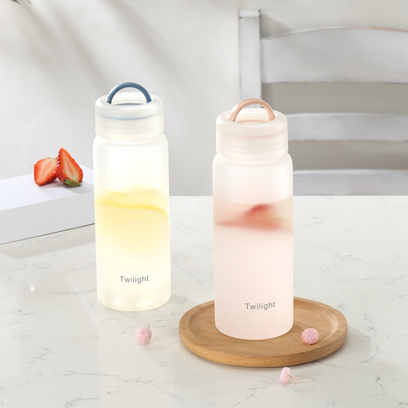Zwei matte Glasflaschen mit farbigen Getraenken, beschriftet mit 'Twilight', eine rosa, die andere gelb, auf einem Marmortisch, daneben Erdbeeren und kleine rosa Blueten.