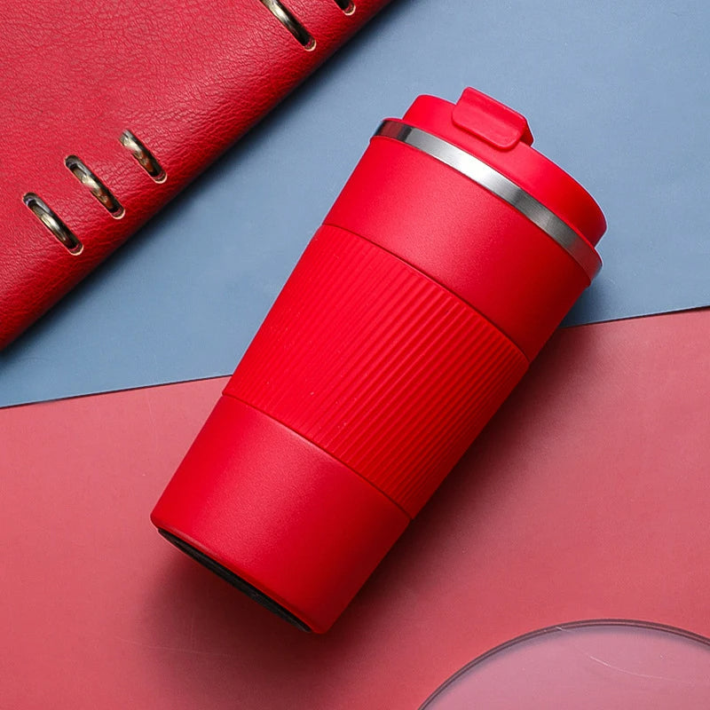 Ein roter Thermobecher liegt auf einer zweifarbigen Unterlage neben einem roten Gegenstand mit Metalloesen.
