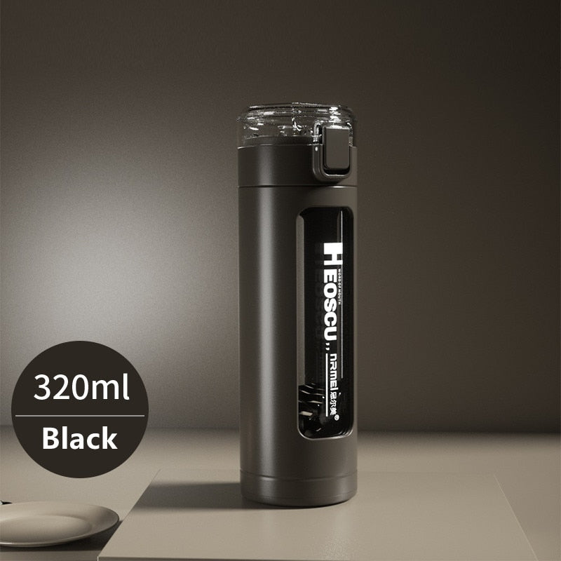 Eine schwarze Glastrinkflasche mit einem Fassungsvermoegen von 320 ml, ausgestattet mit einem aufklappbaren Deckel und einem eingebauten Strohhalm. Die Flasche steht auf einer cremefarbenen Oberflaeche vor einem einfarbigen gruenen Hintergrund.