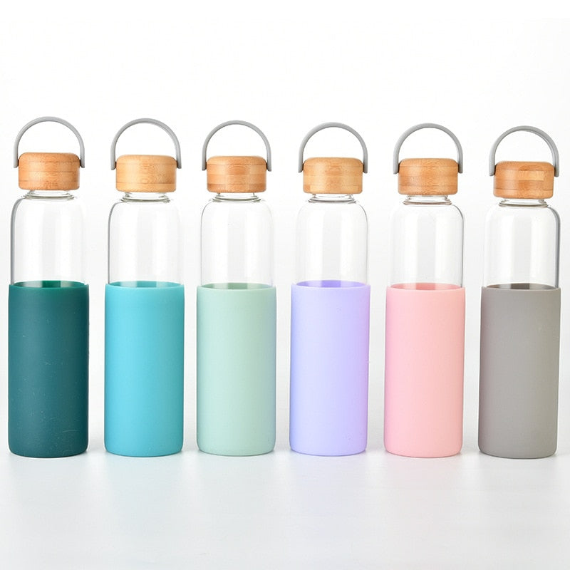 Reihe von farbigen Glasflaschen mit Bambusdeckel und Silikonschutzhuellen auf weißem Hintergrund.