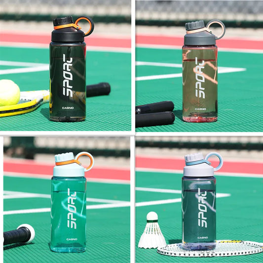 Vier verschiedene Sporttrinkflaschen in verschiedenen Farben auf einem Sportplatz. Jede Flasche hat das Wort "SPORT" aufgedruckt und ist mit einem Henkel und einem Schraubverschluss ausgestattet.