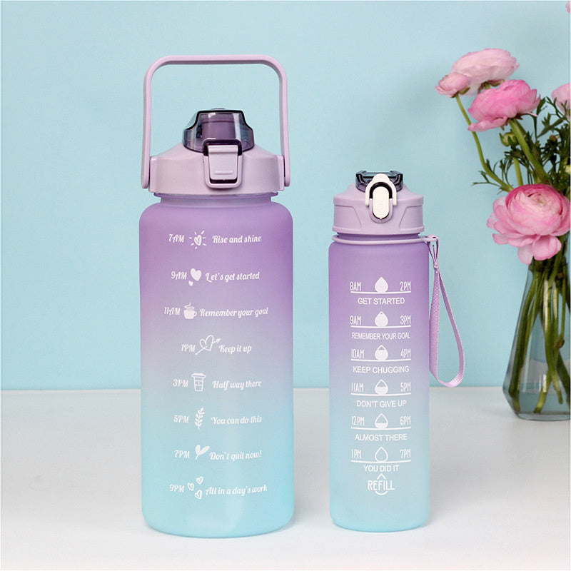 Zwei verlaufsfarbene Sporttrinkflaschen, eine groesser in Violett und Blau, die andere kleiner in Violett und Blau, mit Zeitmarkierungen, vor einem pastellblauen Hintergrund mit rosa Blumen.