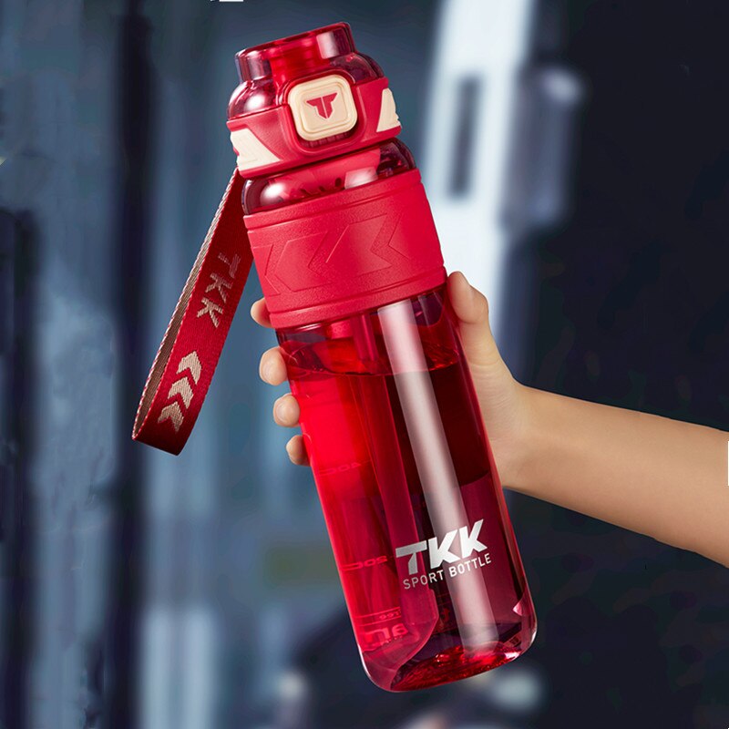 Eine Hand haelt eine transparente rote Sporttrinkflasche mit der Aufschrift TKK und einem offenen Deckel, aus dem eine Schlaufe ragt.