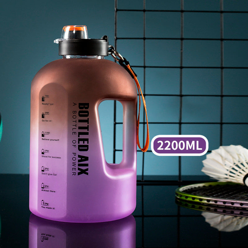 Eine große Sporttrinkflasche in Ombre-Farbe von Braun zu Lila mit einem Fassungsvermoegen von 2200ml, motivierenden Zeitmarkierungen und einer Badminton-Ausruestung im Hintergrund.
