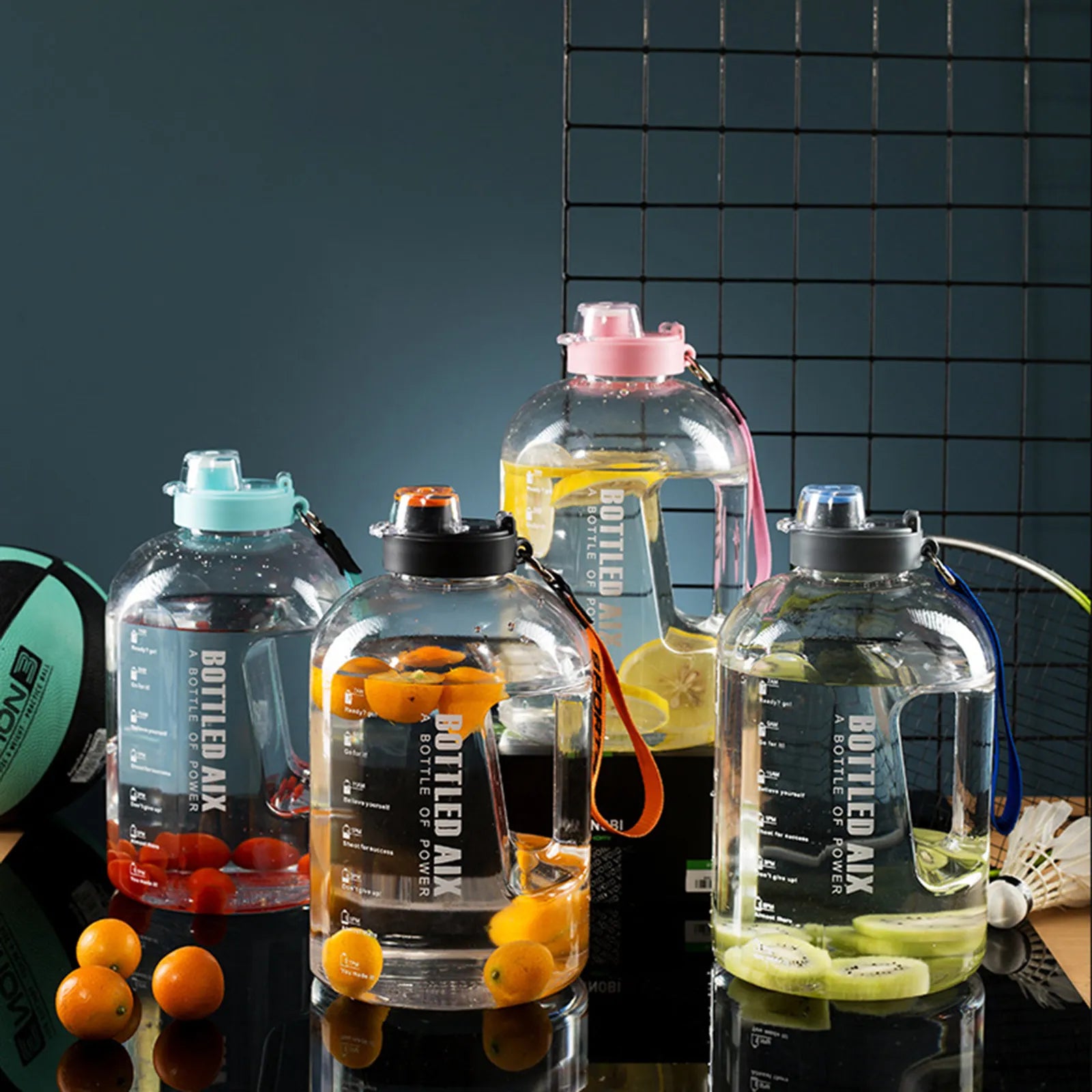 Vier transparente Sporttrinkflaschen gefuellt mit Obst und Wasser, darunter Orangen und Kiwis, auf einer dunklen Reflexionsflaeche mit einem schwarzen Gitter und Sportutensilien im Hintergrund.