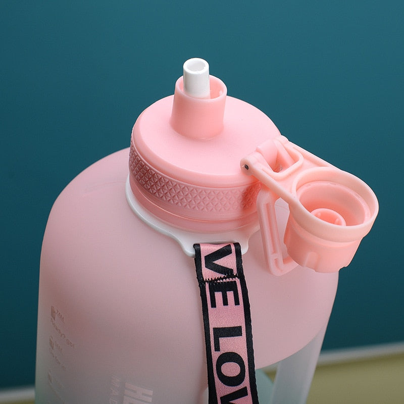 Nahaufnahme des Deckels einer grossen pinkfarbenen Sporttrinkflasche mit einem Strohhalm und einem Sicherheitsverschluss. An der Flasche befestigt ist ein Band mit der Aufschrift "LOVE".