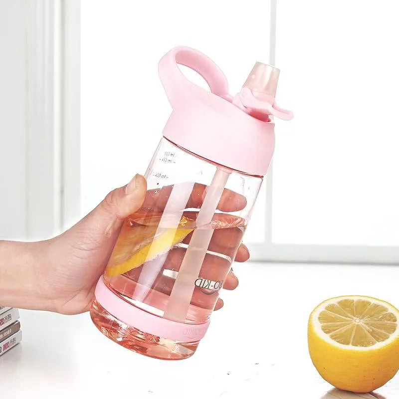 Eine Hand haelt eine transparente, pinkfarbene Trinkflasche mit Strohhalm, gefuellt mit Wasser und Zitronenscheiben, neben einer halbierten Zitrone.