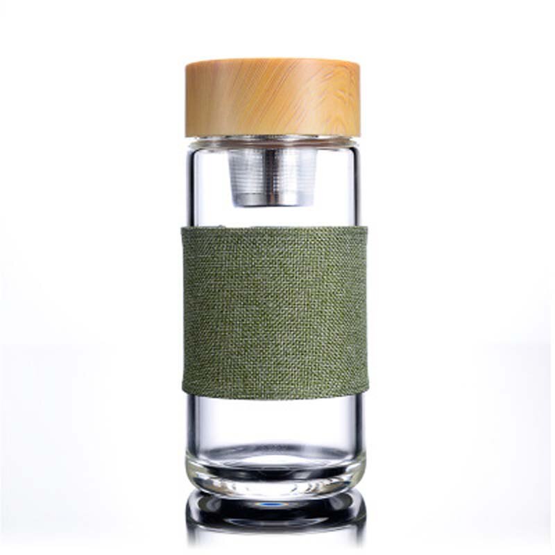 Eine transparente Glas-Trinkflasche mit einem Teesieb und einem Bambusdeckel, umgeben von einem gruenen Stoffband, vor einem weissen Hintergrund.