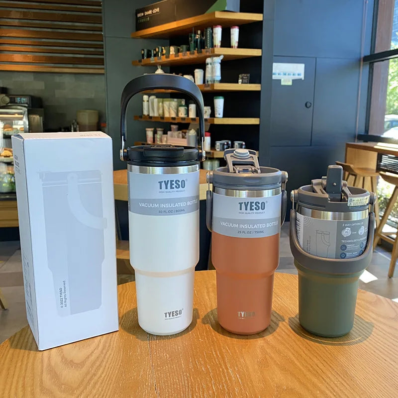 Drei farbige Thermosflaschen auf einem Tisch in einem Café, daneben eine Verpackungsbox. Die Flaschen sind teilweise geueffnet, um die Trinkmechanismen zu zeigen.