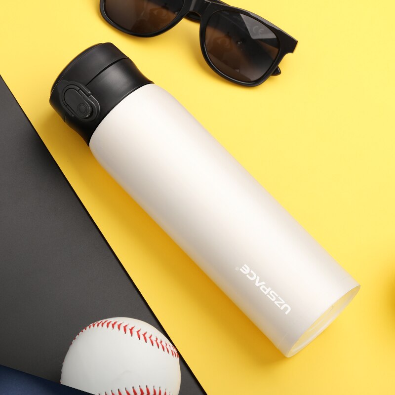 Eine weiße Edelstahl-Thermosflasche mit einem schwarzen Deckel, neben einer Sonnenbrille und einem Baseball auf einem gelben und grauen Hintergrund.