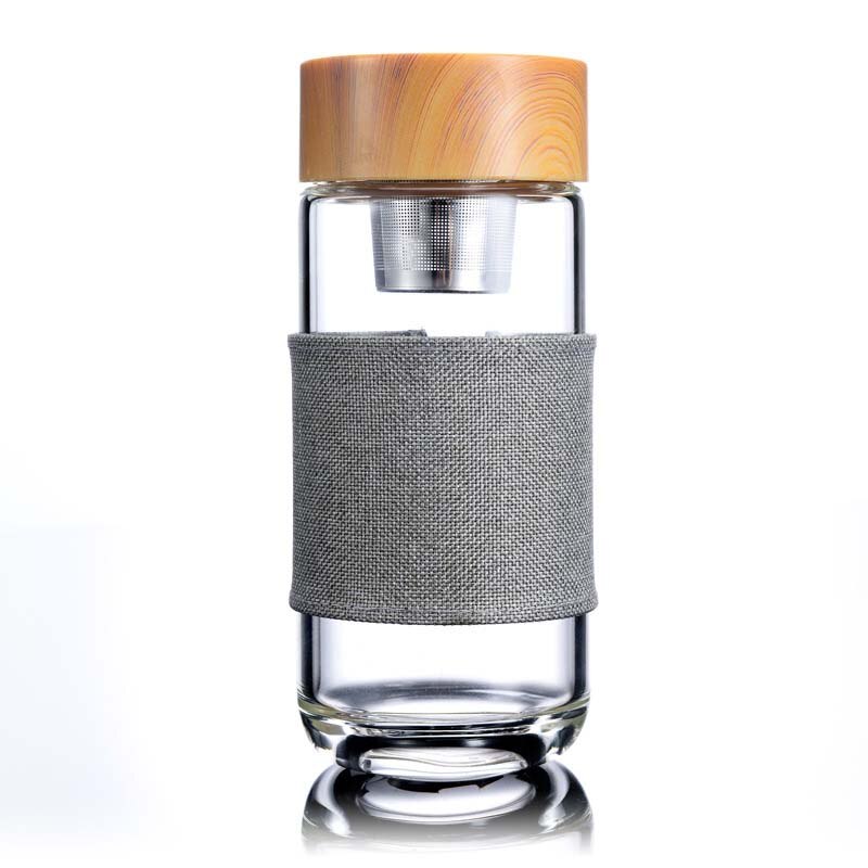 Eine transparente Glas-Trinkflasche mit einem Teesieb und einem Bambusdeckel, umgeben von einem grauen Stoffband, vor einem weissen Hintergrund.