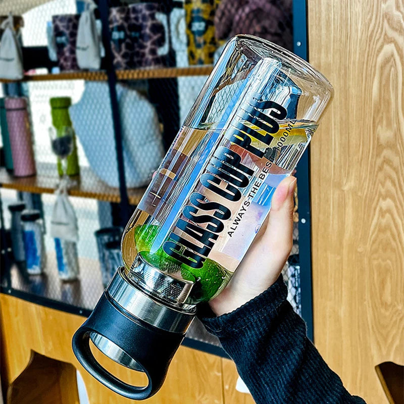 Eine Hand haelt eine transparente Glastrinkflasche mit schwarzer Aufschrift 'GLASS CUP PLUS'. Im Inneren der Flasche sind Limettenscheiben und Minzblaetter zu sehen. Im Hintergrund ist ein Regal mit verschiedenen Trinkflaschen zu erkennen.