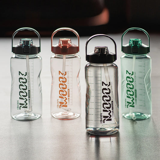 Eine Gruppe von vier durchsichtigen Sportflaschen mit Zeitmarkierungen auf der Seite. Jede Flasche hat einen farbigen Deckel und Tragegriff – schwarz, rot, violett und grün – und die Aufschrift "2000ML" mit einem Zusatztext darunter. Sie sind auf einer reflektierenden Oberfläche platziert.