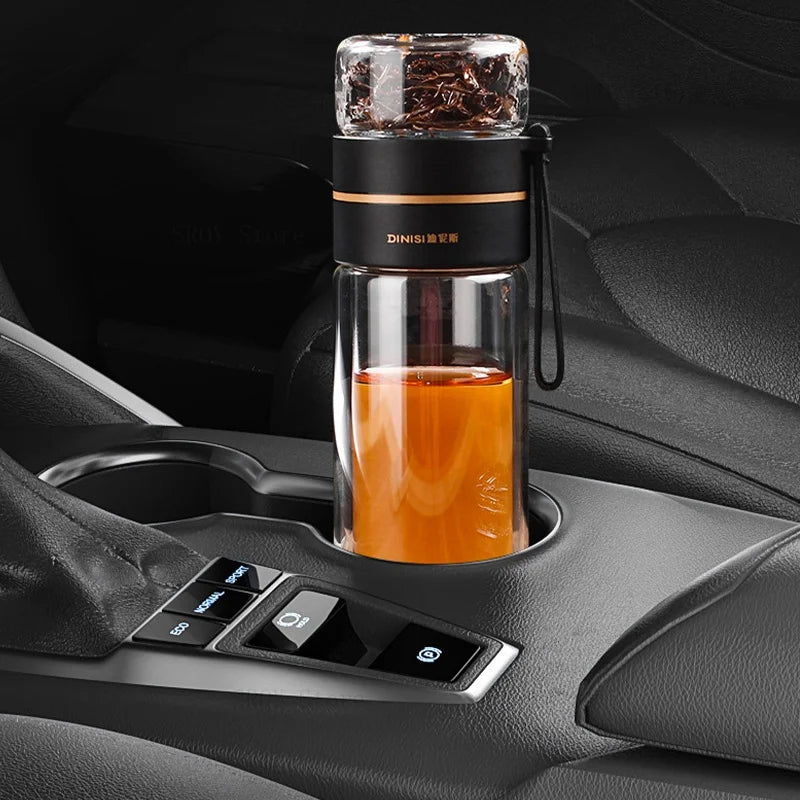 Eine elegante, doppelwandige Glasflasche mit Tee befindet sich im Getraenkehalter eines Autos, das Interieur ist in schwarz gehalten.