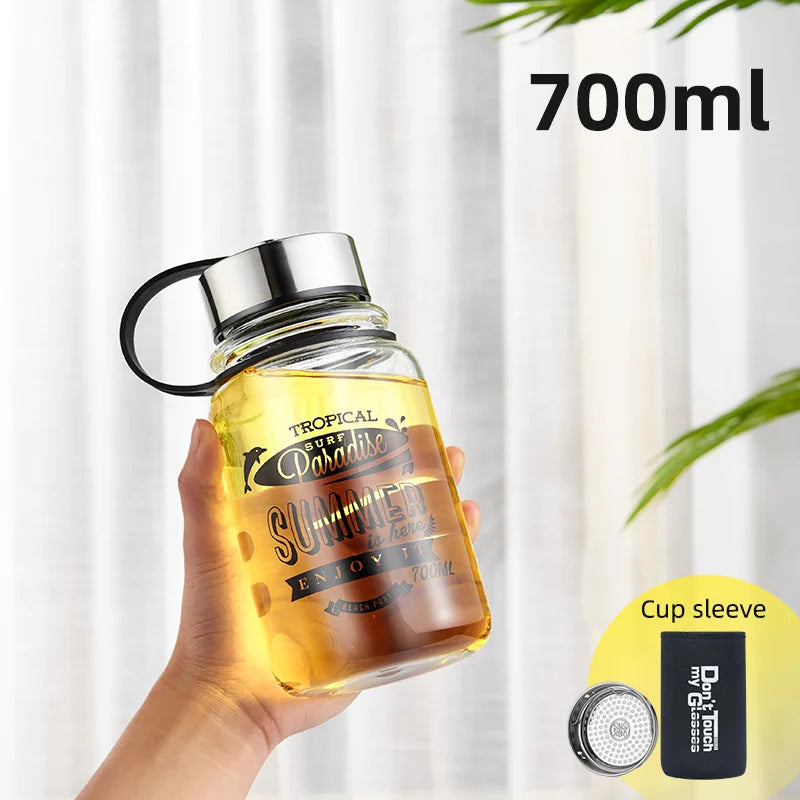 Eine handgehaltene gelbe Glaswasserflasche mit einem Fassungsvermoegen von 700 ml. Auf der Flasche ist ein sommerliches Design mit den Worten "Tropical Surf Paradise SUMMER" und "ENJOY IT" gedruckt. Zusaetzlich ist ein "Cup sleeve" abgebildet.