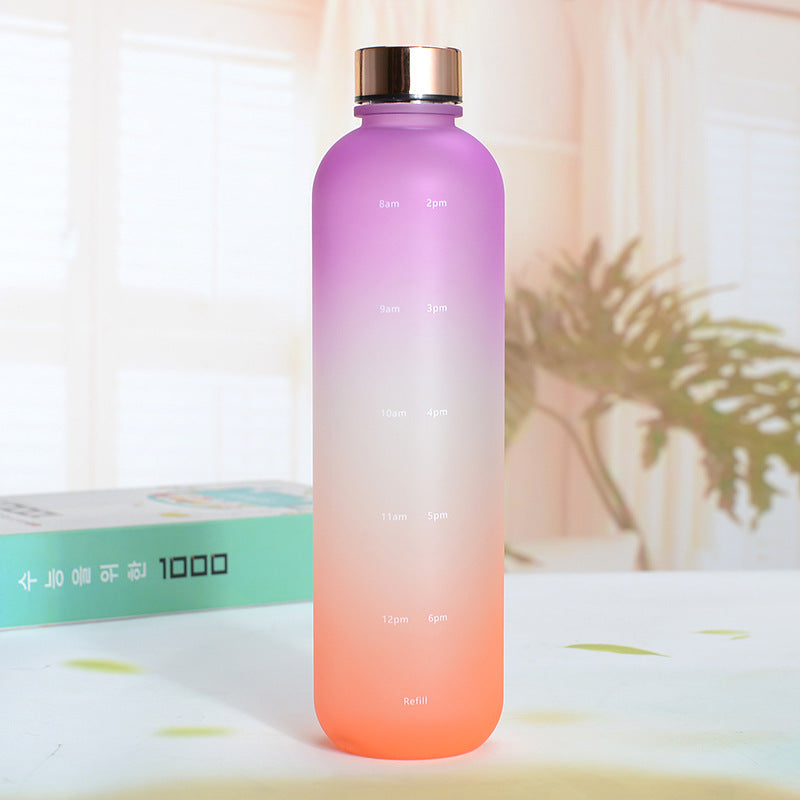 Eine Trinkflasche mit einem Farbverlauf von Violett zu Orange am unteren Ende und einem silbernen Deckel. Die Flasche hat weisse Zeitmarkierungen auf der Seite. Sie steht auf einer Oberflaeche mit einer unscharfen, hellen Umgebung und einer Pflanze im Hintergrund.