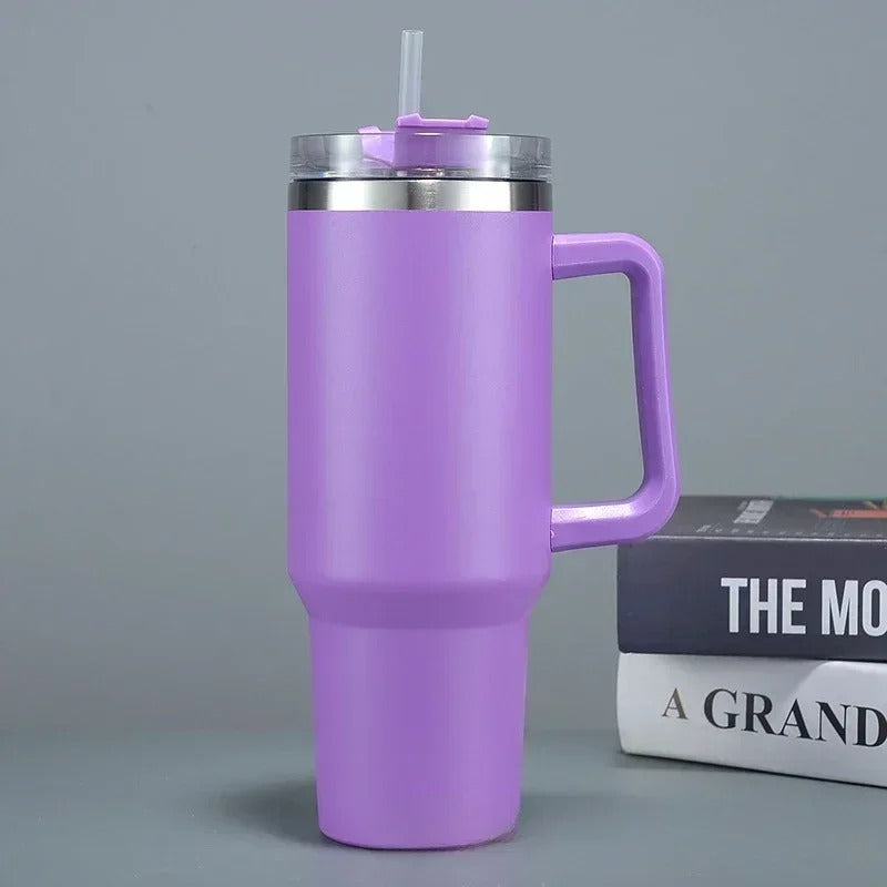Eine violette Thermosflasche mit Strohhalm und einem großen Griff, platziert neben einem Buch auf einem grauen Hintergrund.