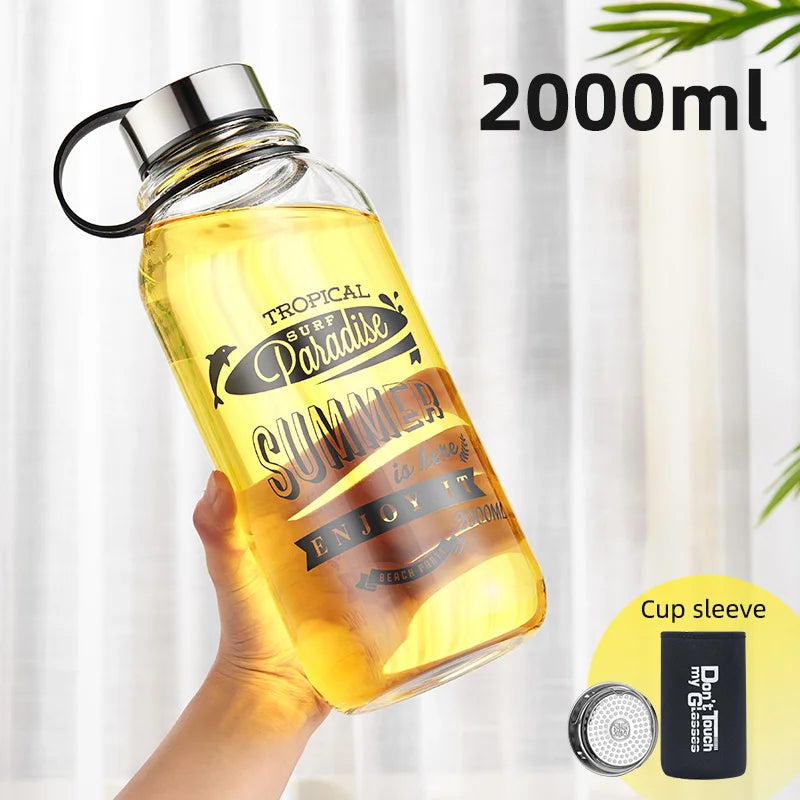 Eine handgehaltene gelbe Glaswasserflasche mit einem Fassungsvermoegen von 2000 ml. Auf der Flasche ist ein sommerliches Design mit den Worten "Tropical Surf Paradise SUMMER" und "ENJOY IT" gedruckt. Zusaetzlich ist ein "Cup sleeve" abgebildet.